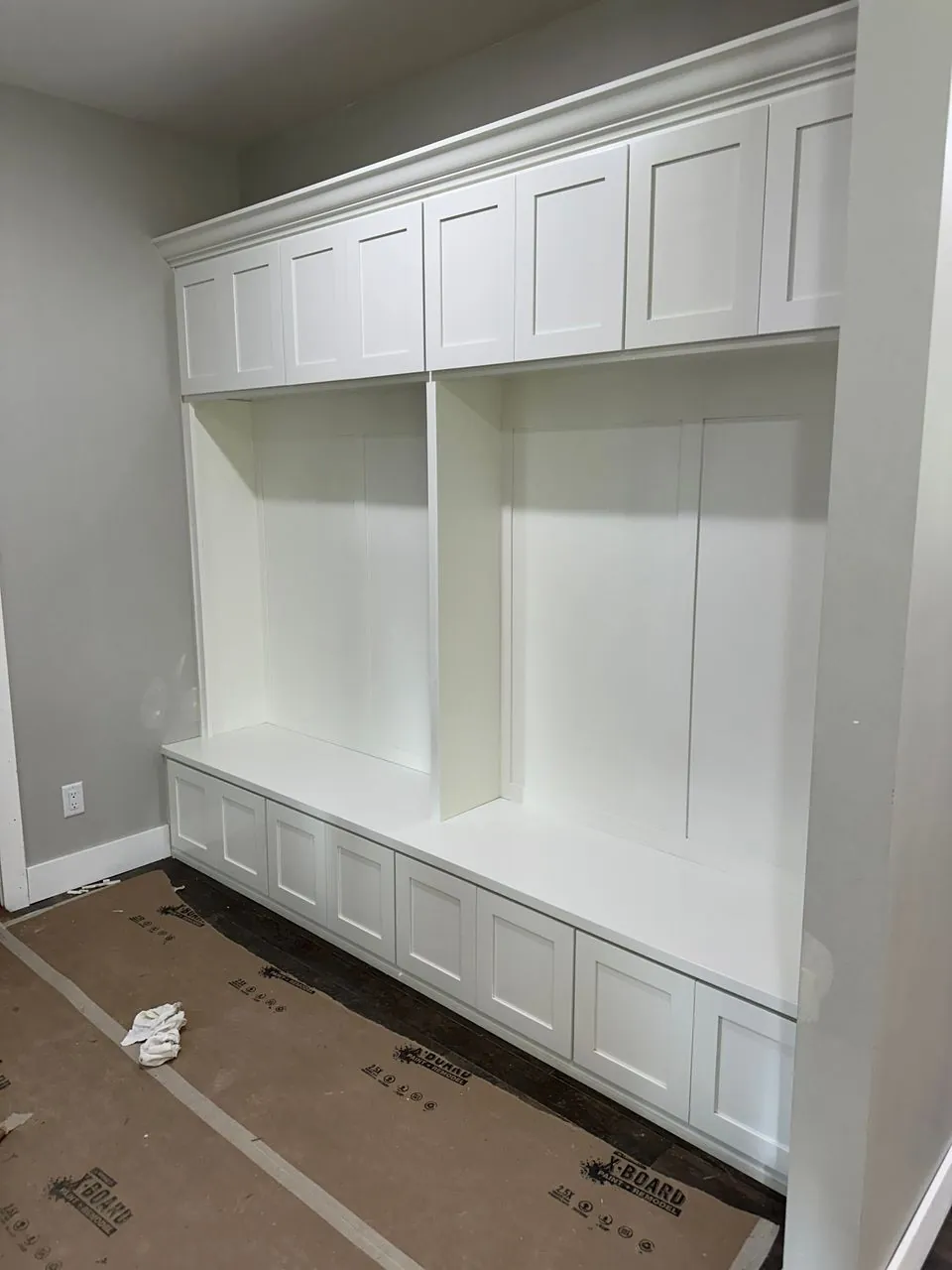 Floor-to-ceiling white Shaker storage wall with upper cabinets, open bays, and built-in bench drawers